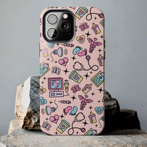 May include: A pink iPhone case with a cute pattern of baby-related icons, including a stethoscope, a baby bottle, a heart, a butterfly, and a baby footprint. The case is designed for an iPhone 13 Pro Max.