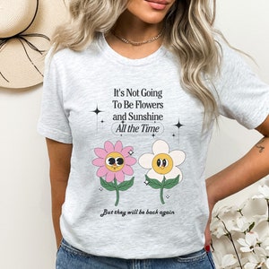 May include: A gray t-shirt with a graphic of two cartoon flowers and the text "It's Not Going To Be Flowers and Sunshine All the Time But they will be back again".