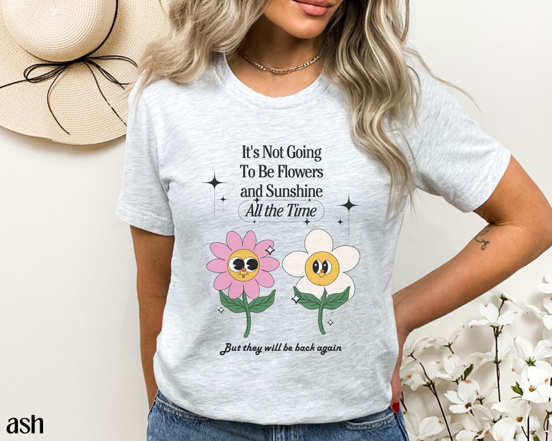 May include: A gray t-shirt with a graphic of two cartoon flowers and the text "It's Not Going To Be Flowers and Sunshine All the Time But they will be back again".