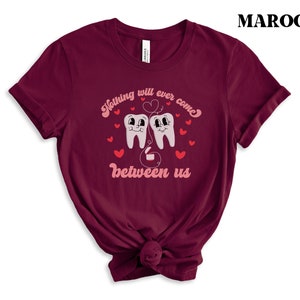 Puede incluir: Camiseta de color granate con un gr&aacute;fico de dos dientes de dibujos animados con corazones y el texto "Nada podr&aacute; interponerse entre nosotros".
