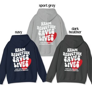 Peut inclure: Trois sweats &agrave; capuche de couleurs marine, gris sport et gris fonc&eacute;. Chaque sweat affiche le texte "HARM REDUCTION SAVES LIVES" en blanc, avec un c&oelig;ur rouge. La phrase "THERE ARE MULTIPLE PATHWAYS TO RECOVERY" est en dessous.