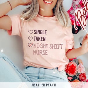 May include: A pink t-shirt with the text "Single, Taken, Night Shift Nurse" with a checkmark next to the last option. The text is in a dark pink color.
