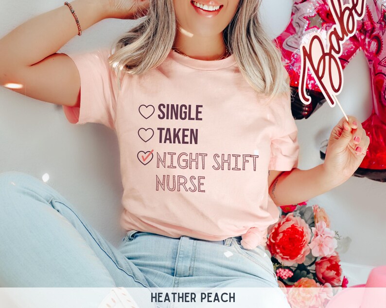 May include: A pink t-shirt with the text "Single, Taken, Night Shift Nurse" with a checkmark next to the last option. The text is in a dark pink color.