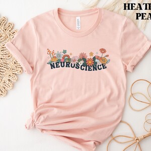 May include: A heather peach t-shirt with a floral design and the text "NEUROSCIENCE" printed on the front.