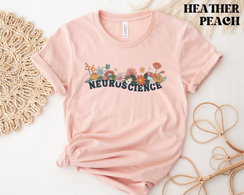 May include: A heather peach t-shirt with a floral design and the text "NEUROSCIENCE" printed on the front.