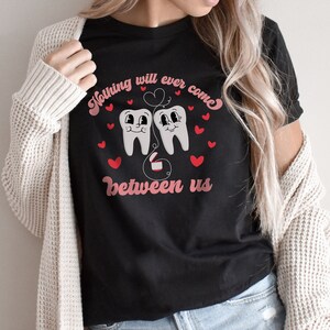 Puede incluir: Camiseta negra con un gr&aacute;fico de dos dientes de dibujos animados con corazones y el texto "Nada podr&aacute; interponerse entre nosotros".