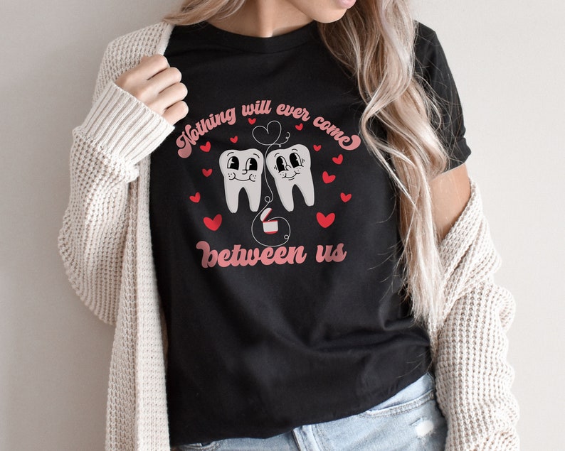Puede incluir: Camiseta negra con un gr&aacute;fico de dos dientes de dibujos animados con corazones y el texto "Nada podr&aacute; interponerse entre nosotros".
