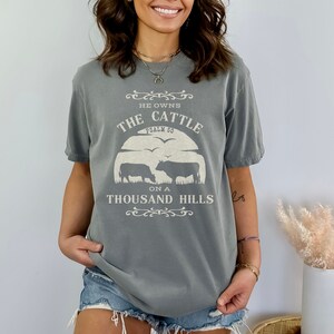 May include: A gray t-shirt with a white graphic that says "He owns the cattle on a thousand hills, Psalm 50". The graphic also includes a silhouette of two cows.