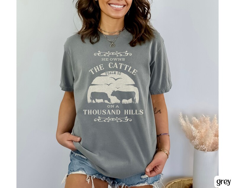 May include: A gray t-shirt with a white graphic that says "He owns the cattle on a thousand hills, Psalm 50". The graphic also includes a silhouette of two cows.