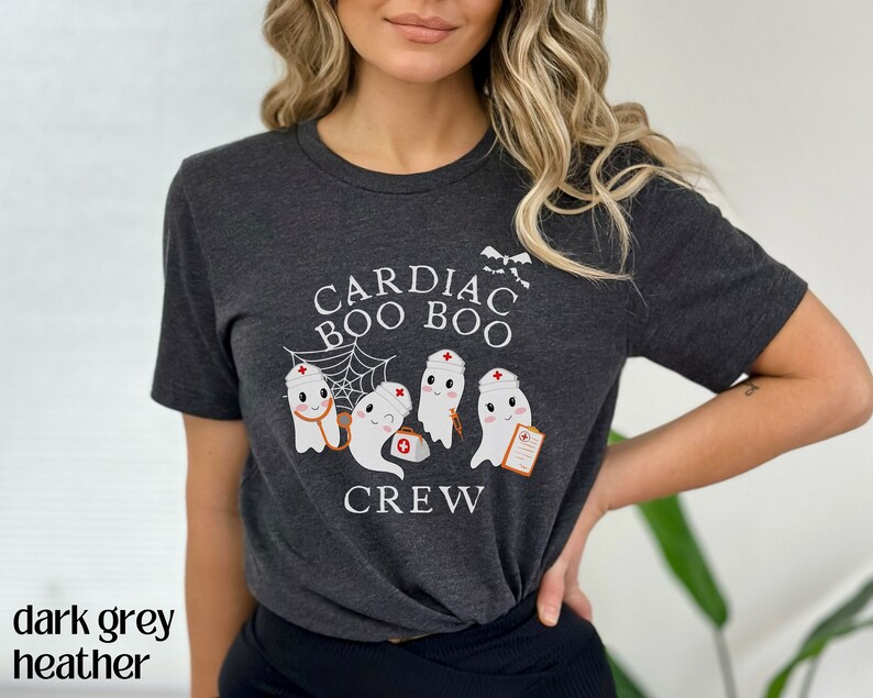 May include: Dark grey heather t-shirt with a graphic of ghosts wearing nurse hats and the text "Cardiac Boo Boo Crew".