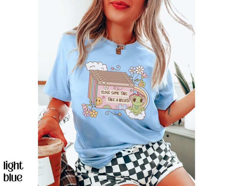 May include: A light blue t-shirt with a graphic of a cartoon frog and the text "Close some tabs, take a breath". The graphic is surrounded by flowers and clouds.