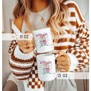 May include: Two white ceramic mugs with a colourful cartoon design. The mugs feature a rainbow, clouds, and two cartoon characters holding drinks. The text on the mugs reads "If you're happy and you know it, sip your tea". The mugs are available in 11 oz and 15 oz sizes.