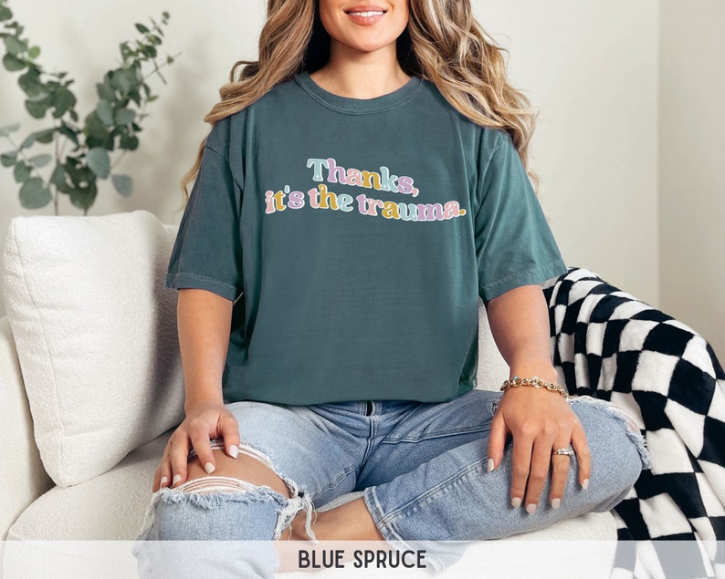 May include: A teal blue t-shirt with the text "Thanks, it's the trauma." in colorful letters.