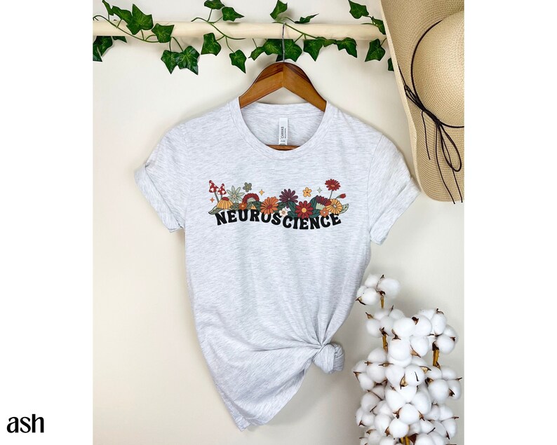 May include: A grey t-shirt with a floral and mushroom design and the word "NEUROSCIENCE" in black lettering.