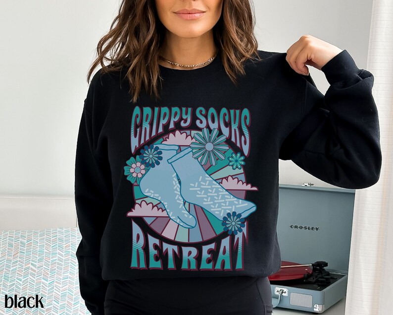 May include: Black sweatshirt with a graphic design of blue socks with a retro-style design and the text "Grippy Socks Retreat".