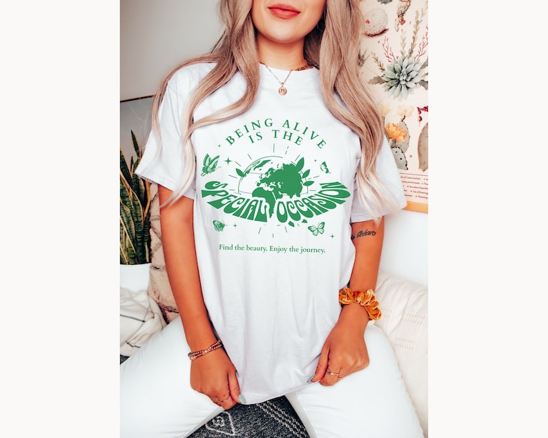 May include: White t-shirt with a green graphic of the Earth with butterflies and the text "Being Alive is the Special Occasion. Find the beauty. Enjoy the journey."