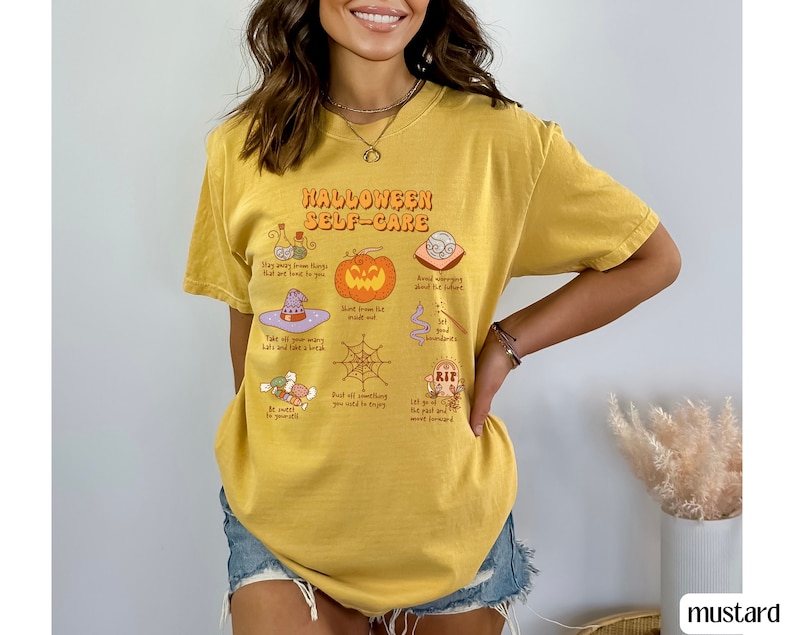 May include: A yellow t-shirt with a graphic print of a Halloween self-care guide. The graphic includes illustrations of a witch's hat, a pumpkin, a spiderweb, and other Halloween-themed items. The text on the shirt reads "Halloween Self-Care".