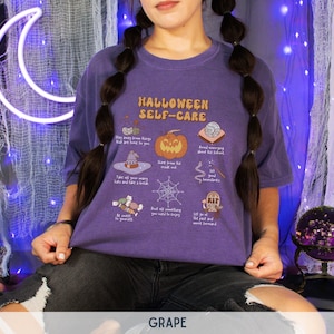 May include: A purple t-shirt with a graphic print of a list of Halloween self-care tips. The text on the shirt reads "Halloween Self-Care".