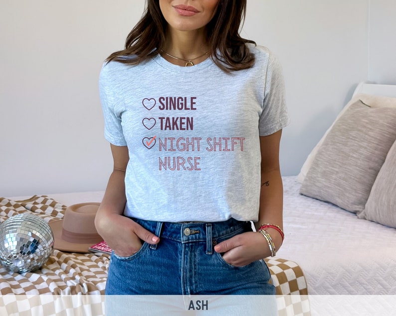 May include: A light gray t-shirt with a pink and maroon graphic that reads "Single, Taken, Night Shift Nurse" with a checkmark next to the last line.