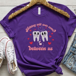 Puede incluir: Camiseta morada con un gr&aacute;fico de dos dientes de dibujos animados con un coraz&oacute;n rosa y el texto "Nada nos separar&aacute; jam&aacute;s".