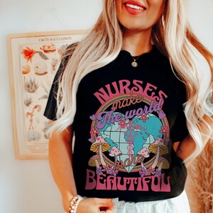 Puede incluir: Camiseta negra con un gr&aacute;fico de arco&iacute;ris y globo terr&aacute;queo. El texto "Nurses make the world more beautiful" est&aacute; impreso en la camiseta.