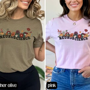 May include: Two women's t-shirts with a floral design and the text "Neuroscience". The shirt on the left is heather olive and the shirt on the right is pink.