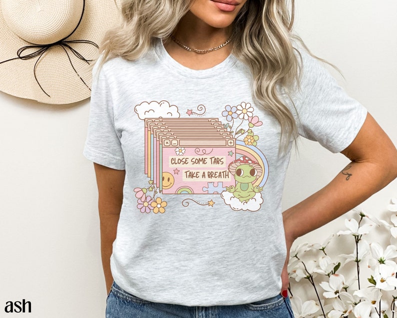 May include: A gray t-shirt with a graphic of a frog wearing a mushroom hat and a cloud with the text "Close some tabs take a breath". The graphic is surrounded by flowers and stars.