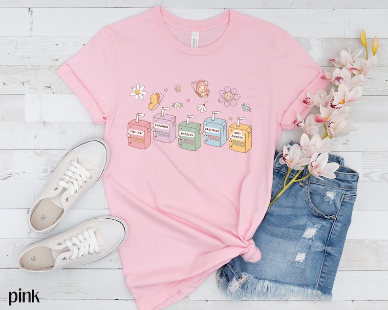 May include: Pink t-shirt with a graphic of colorful juice boxes with text that reads "Self Love Punch", "Empathy Punch", "Gratitude Punch", "Optimism Punch", and "Anti-Anxiety Punch".