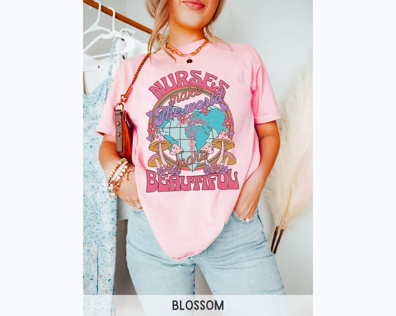 Puede incluir: Camiseta rosa con un gr&aacute;fico de un globo terr&aacute;queo con setas y flores. El texto de la camiseta dice "Nurses make the world more beautiful."
