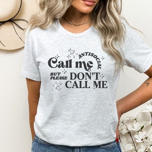 Puede incluir: Una camiseta gris con un gr&aacute;fico negro que dice "Call me antisocial but please don't call me".