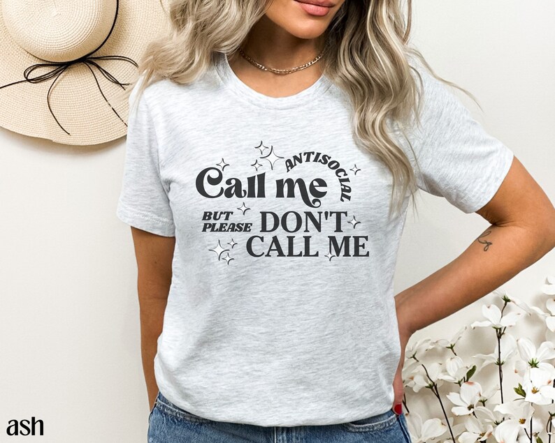 Puede incluir: Una camiseta gris con un gr&aacute;fico negro que dice "Call me antisocial but please don't call me".