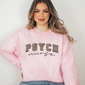 May include: Light pink sweatshirt with the text "PSYCH nurse" in black script and leopard print lettering. The words "light pink" are in the bottom left corner.