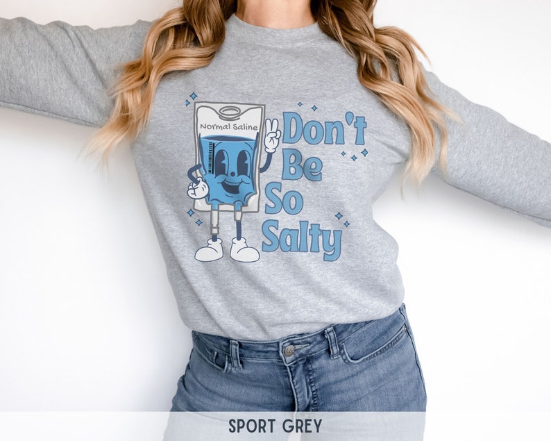 Op de afbeelding: Een grijs sweatshirt met een cartoonillustratie van een infuuszak met de tekst "Normal Saline" en de zin "Don't Be So Salty".