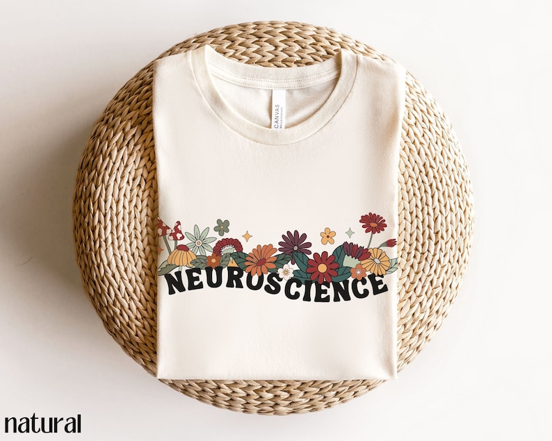 May include: A natural colored t-shirt with a floral design and the word "NEUROSCIENCE" in black lettering.