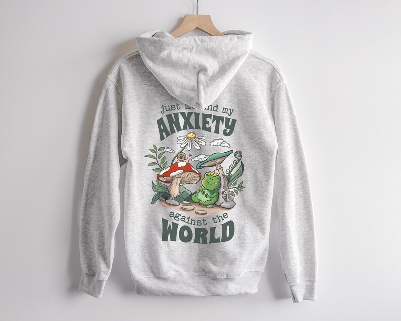 May include: Gray hooded sweatshirt with a green frog, mushroom, and snail graphic. The text "Just me and my anxiety against the world" is printed on the back.