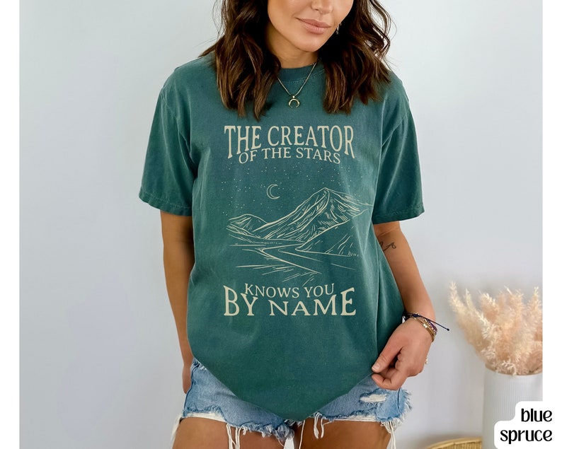 May include: A teal green t-shirt with a mountain landscape graphic and the text "The Creator of the Stars Knows You By Name".