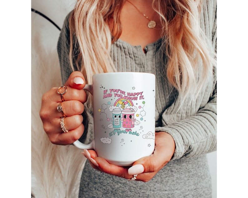 May include: White ceramic mug with a colourful illustration of two cartoon coffee cups with the text "If you're happy and you know it, it's your meds."