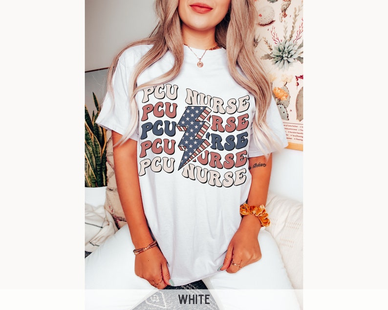 K&ouml;nnte beinhalten: Wei&szlig;es T-Shirt mit einem Grafikdruck eines Blitzes mit einem amerikanischen Flaggenmuster und dem Text "PCU NURSE", der in einem gestapelten Muster wiederholt wird.