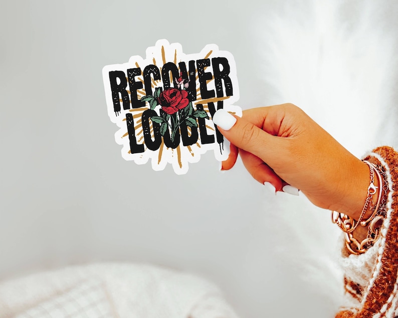 May include: A white sticker with black text that reads "RECOVER LOUDLY" with a red rose and gold accents.