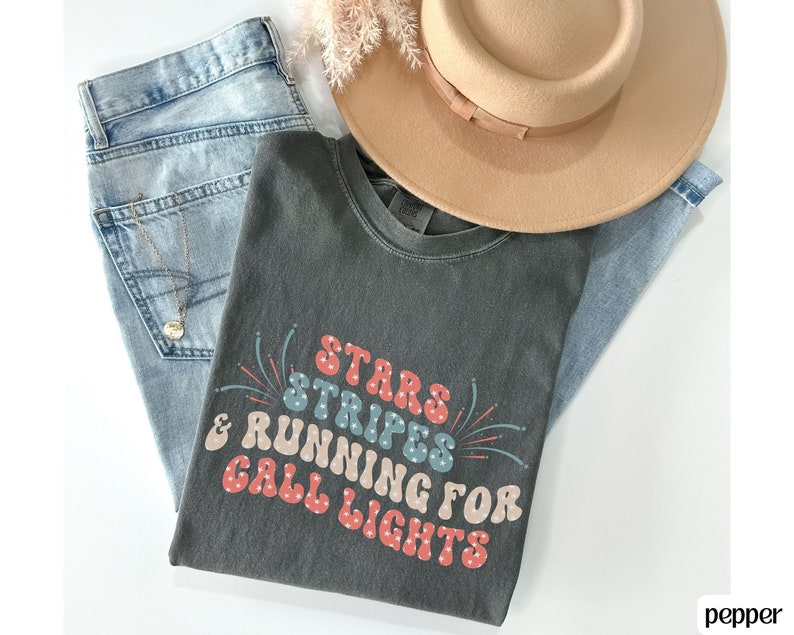May include: A dark gray t-shirt with a retro-style graphic that says "Stars Stripes & Running for Call Lights" in red, blue, and white. The graphic includes fireworks.