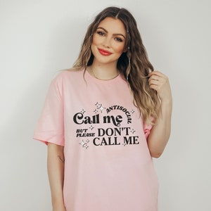 Puede incluir: Camiseta rosa con un gr&aacute;fico negro que dice "Call me Antisocial But Please Don't Call Me".