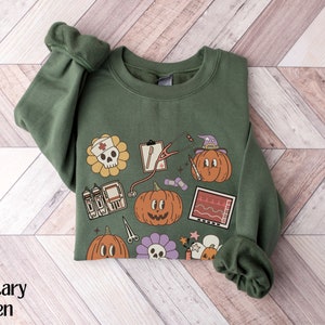 May include: A green sweatshirt with a Halloween-themed design featuring pumpkins, a skull, a stethoscope, and other medical symbols. The text "Boo" is printed on the sweatshirt.