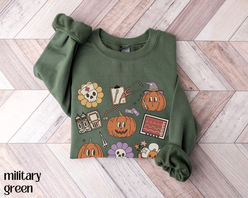 May include: A green sweatshirt with a Halloween-themed design featuring pumpkins, a skull, a stethoscope, and other medical symbols. The text "Boo" is printed on the sweatshirt.