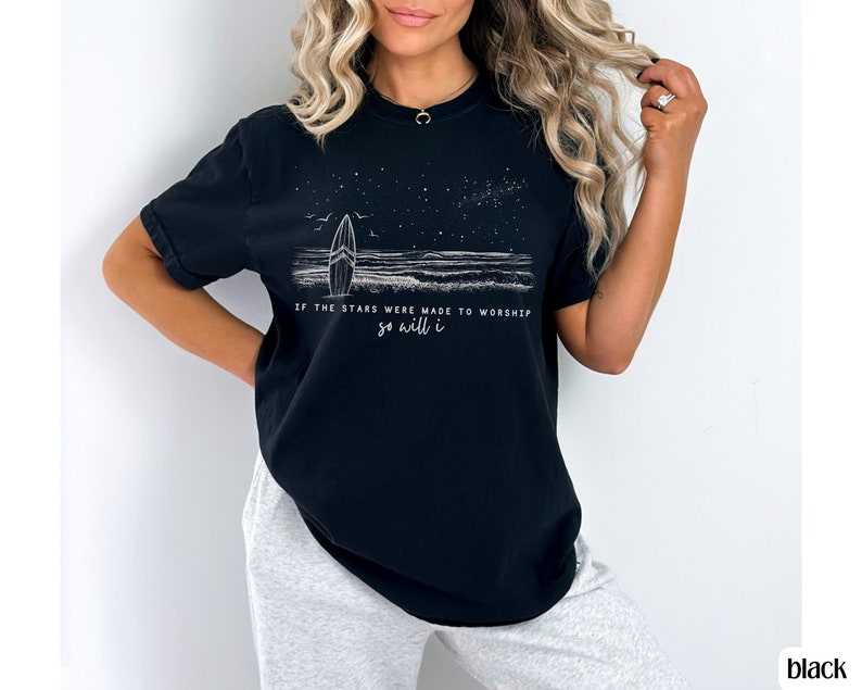Puede incluir: Camiseta negra con un gr&aacute;fico blanco de una tabla de surf y estrellas con el texto "Si las estrellas fueron hechas para adorar, yo tambi&eacute;n lo har&eacute;."