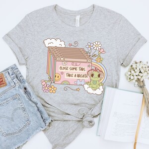 May include: Gray t-shirt with a cartoon frog and the text "Close some tabs take a breath". The design features a stack of browser tabs with a rainbow and a smiley face.