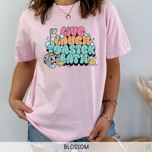 Pu&ograve; includere: Maglietta rosa con una grafica di una doccia di cartoni animati, bolle e il testo "Live Laugh Toaster Bath".