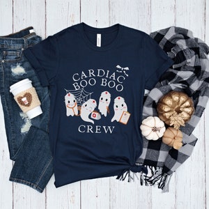 May include: A navy blue t-shirt with a graphic of four ghosts dressed as nurses. The text on the shirt reads "Cardiac Boo Boo Crew".