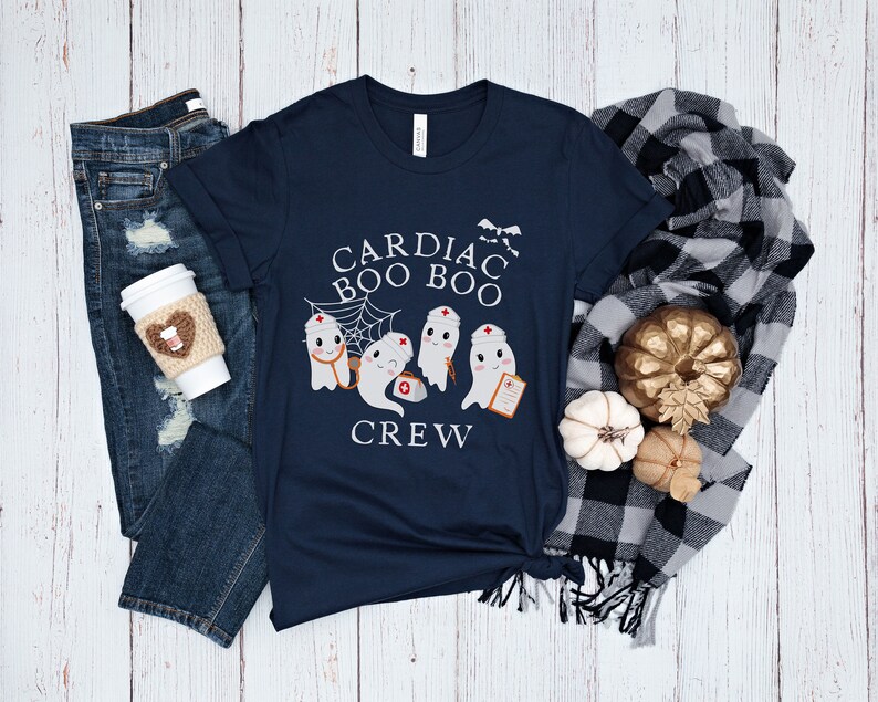 May include: A navy blue t-shirt with a graphic of four ghosts dressed as nurses. The text on the shirt reads "Cardiac Boo Boo Crew".