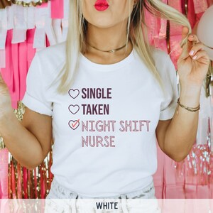 May include: White t-shirt with a pink heart design and the text "SINGLE TAKEN NIGHT SHIFT NURSE" with a checkmark next to "NIGHT SHIFT NURSE".