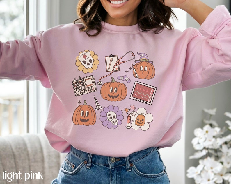 May include: Light pink sweatshirt with a graphic print of various Halloween-themed medical illustrations, including pumpkins, a stethoscope, a skull, and a heart monitor.